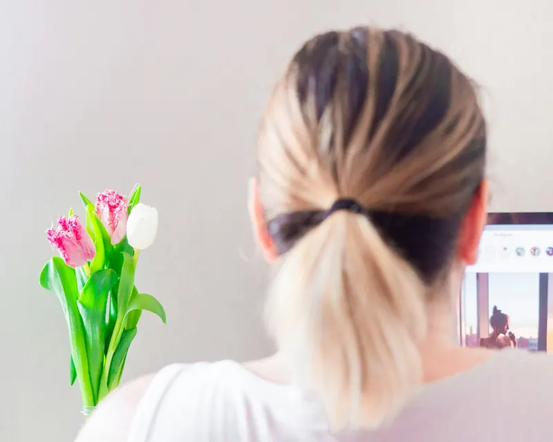 Femme de dos devant son écran, bouquet de tulipes roses sur le bureau